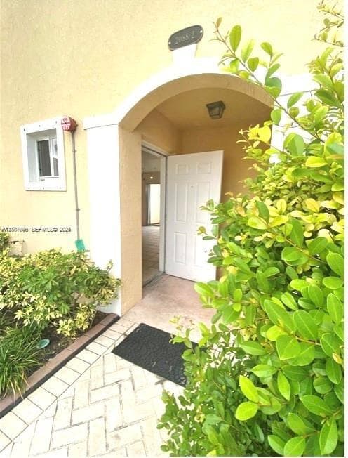 Covered entryway featuring a stucco archway, herringbone-patterned paved walkway, and built-in exterior lighting