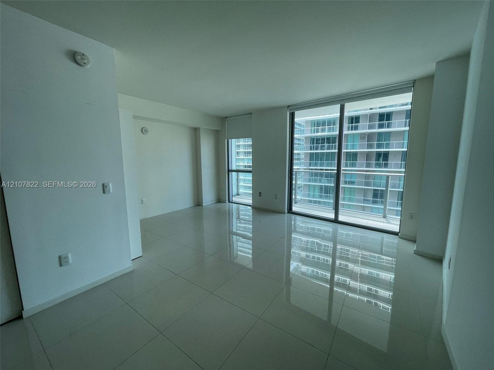 Large-format tile flooring, expansive floor-to-ceiling glass windows, and sliding glass door access to a balcony
