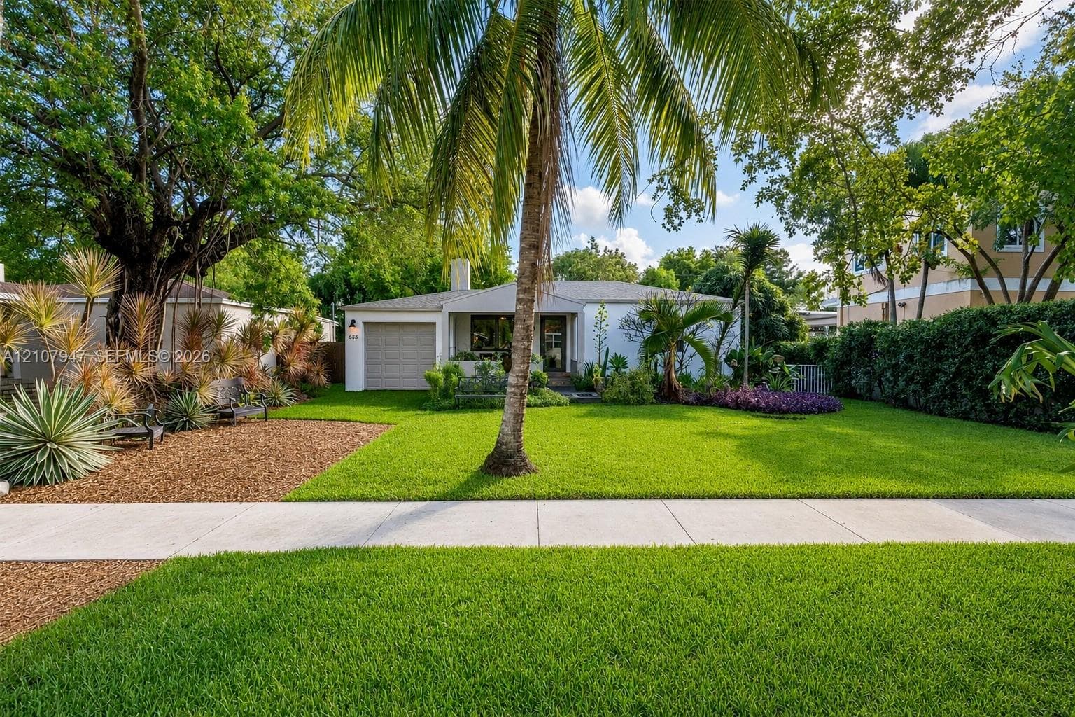 Single-story residence featuring a light-toned exterior, an attached one-car garage, manicured lawn, palm tree, and mature landscaping