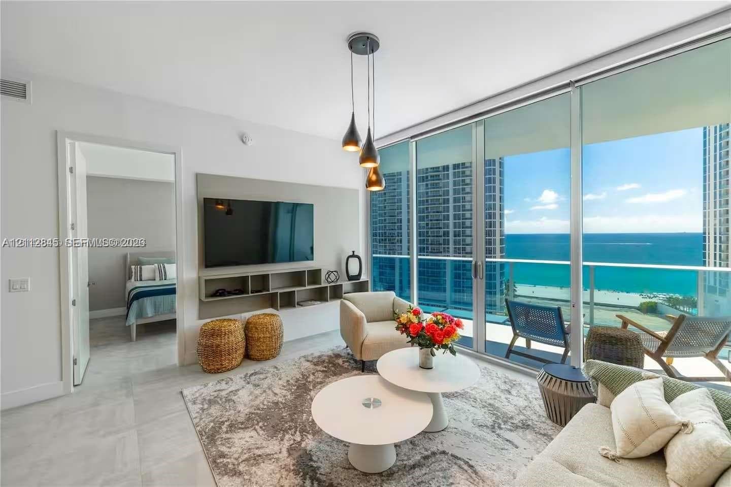 Floor-to-ceiling windows with oceanfront exposure, custom built-in media shelving, pendant lighting, and large-format tile flooring